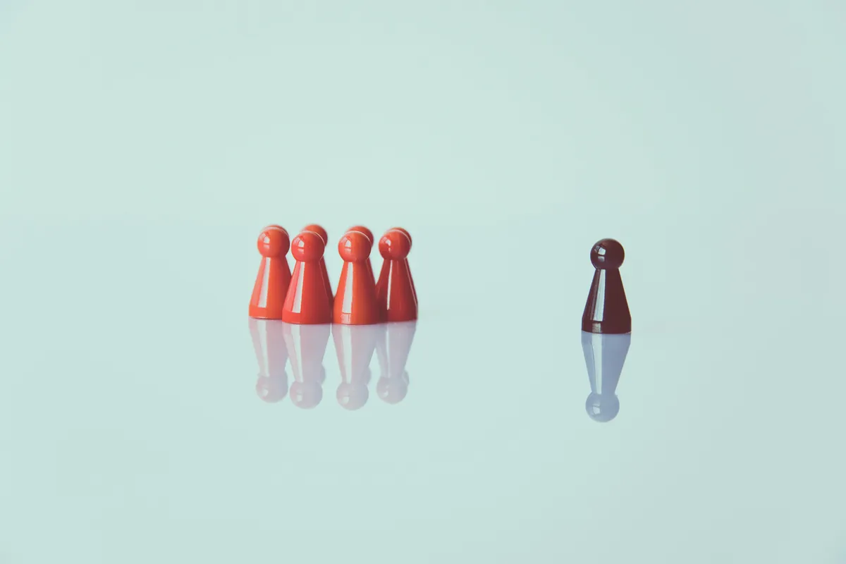 Eine dunkle Spielfigur steht abseits einer Gruppe roter Spielfiguren