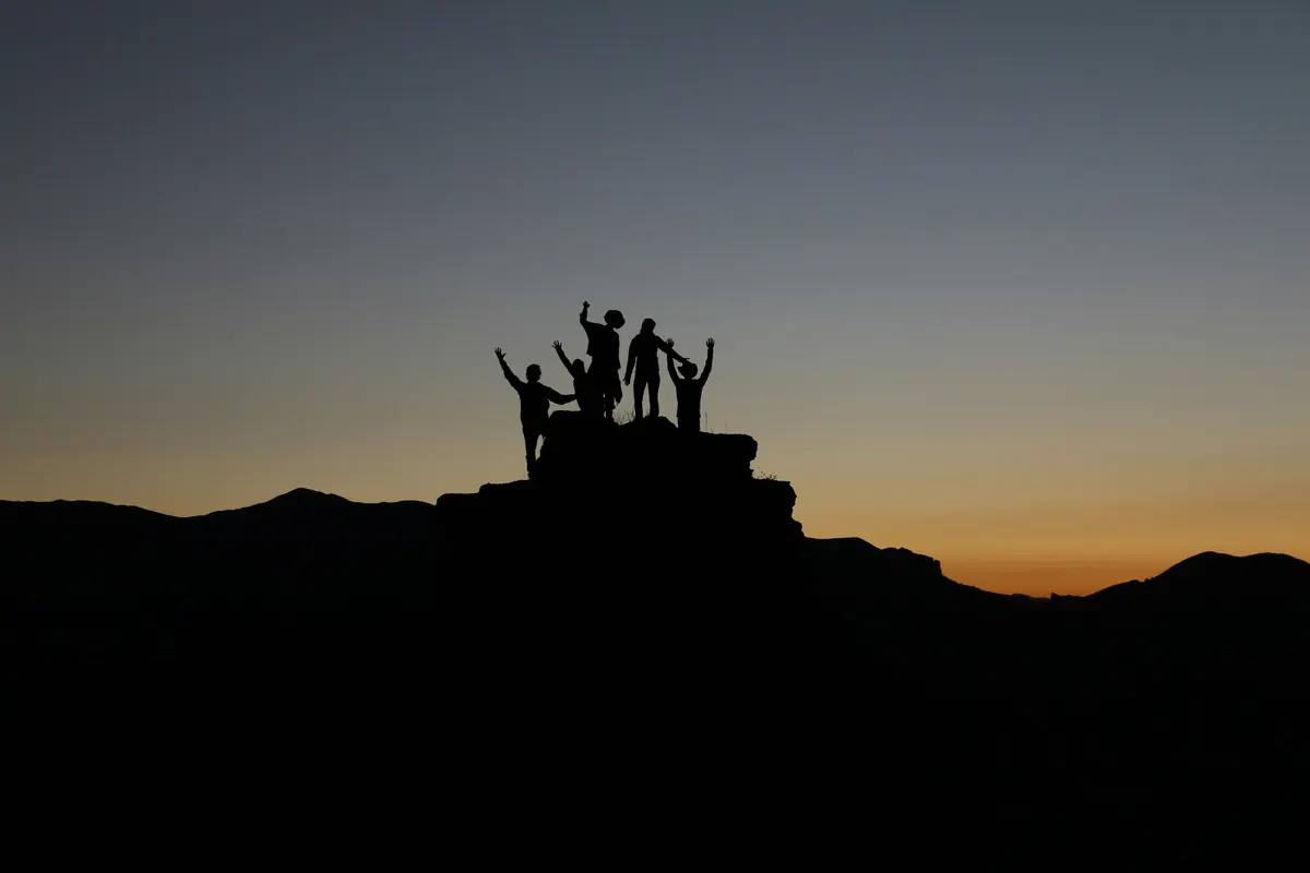 Eine Gruppe steht mit erhobenen Armen auf einem Felsen vor dem Abendhimmel
